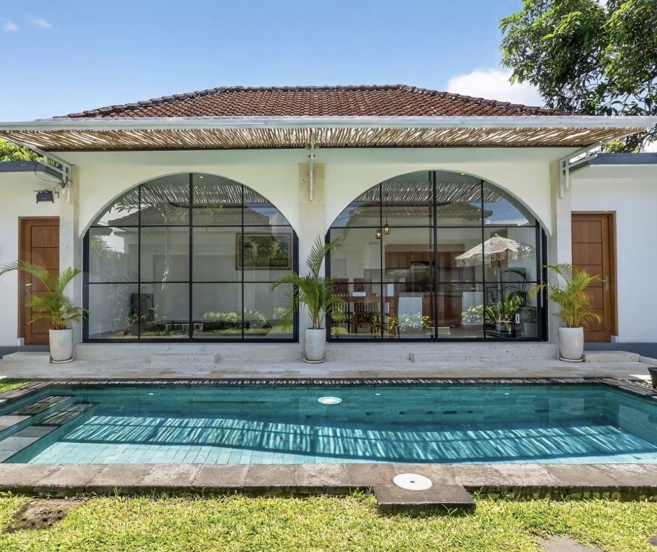 Villa Archway in Kuta, Bali: private swimming pool in front of a white villa with two tall arched windows and a shaded veranda.